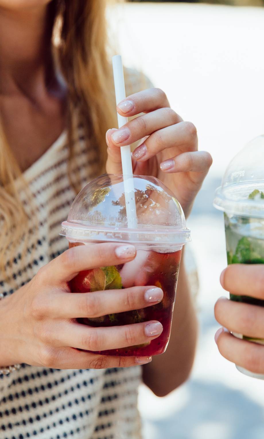 Young woman and man holding cups with cocktail, enjoying the summer. Close-up view.